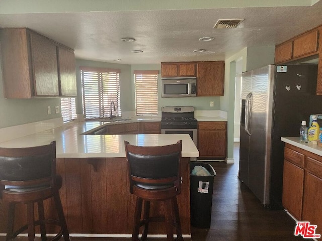 kitchen featuring kitchen peninsula, appliances with stainless steel finishes, a kitchen bar, dark hardwood / wood-style floors, and sink