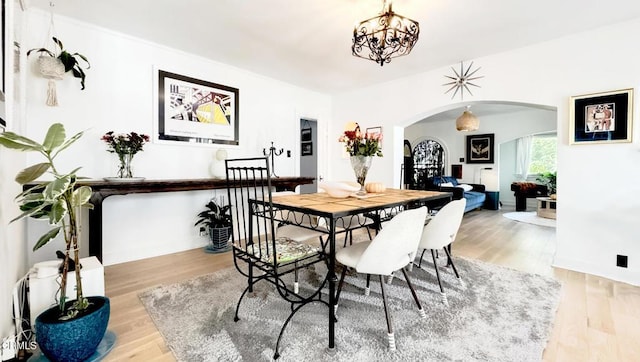 dining room featuring arched walkways, baseboards, light wood finished floors, and a notable chandelier