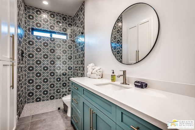 bathroom featuring a tile shower, vanity, tile walls, tile patterned flooring, and toilet