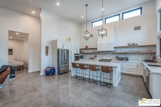 kitchen featuring sink, a towering ceiling, a kitchen bar, white cabinets, and appliances with stainless steel finishes