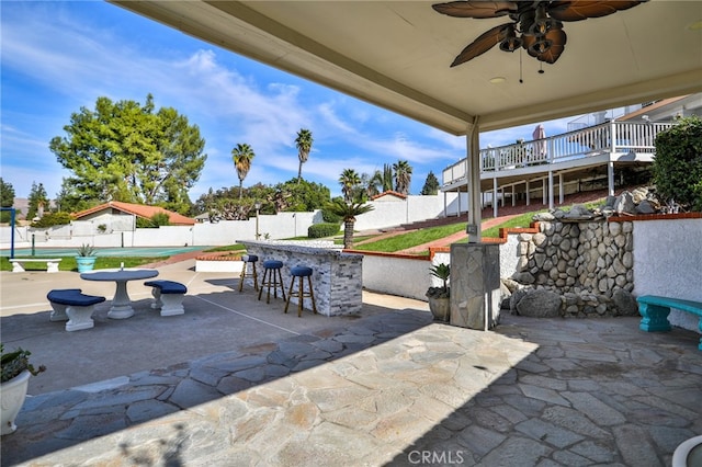 view of patio with ceiling fan, exterior bar, and a wooden deck