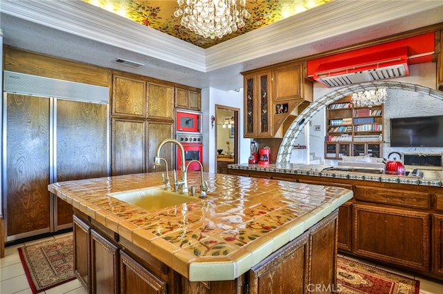 kitchen with an island with sink, sink, ornamental molding, a chandelier, and light tile patterned flooring