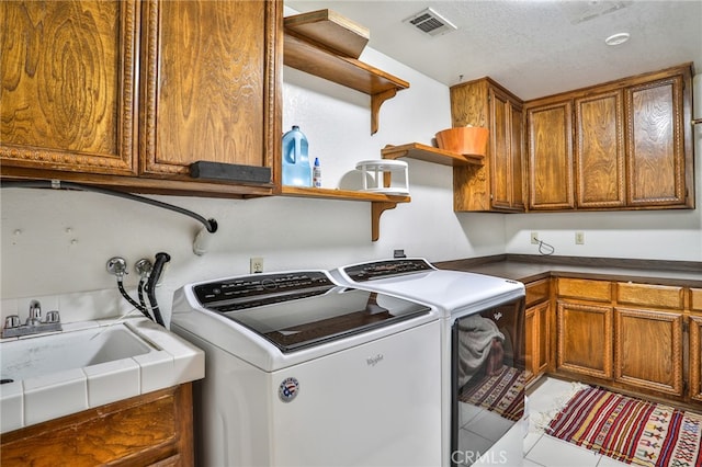 laundry room featuring sink, light tile patterned flooring, washing machine and clothes dryer, a textured ceiling, and cabinets