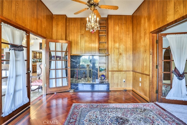 unfurnished living room featuring ceiling fan with notable chandelier, wood walls, and dark parquet floors