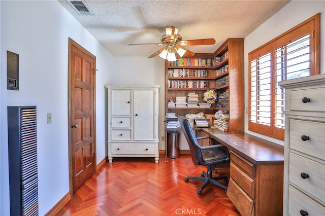 home office featuring built in desk, dark parquet floors, a textured ceiling, and ceiling fan