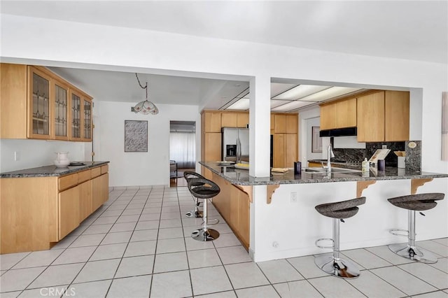 kitchen with kitchen peninsula, a kitchen breakfast bar, stainless steel fridge, dark stone countertops, and hanging light fixtures