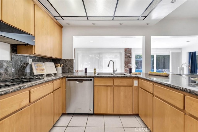 kitchen with sink, dark stone countertops, light tile patterned floors, range hood, and appliances with stainless steel finishes