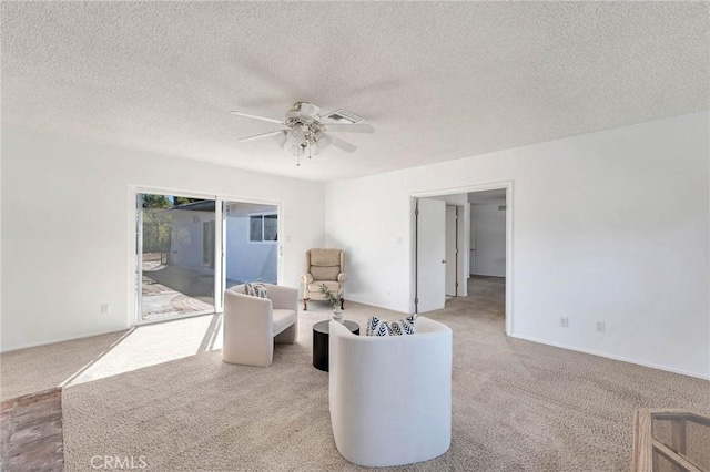 living area featuring light carpet, a textured ceiling, and ceiling fan