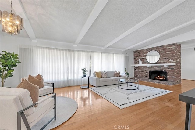 living room with vaulted ceiling with beams, hardwood / wood-style flooring, a brick fireplace, and a notable chandelier