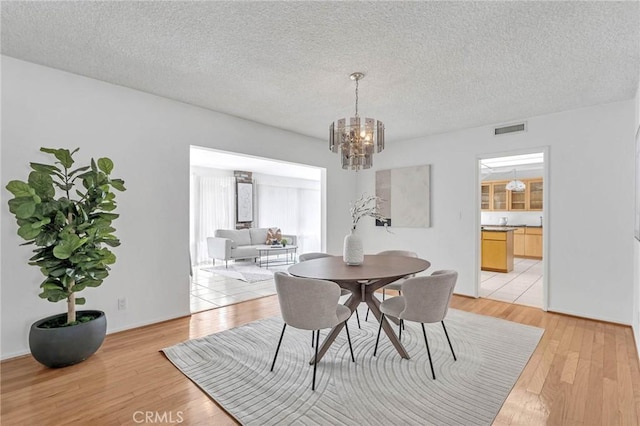 dining room with light wood-type flooring, a textured ceiling, and a chandelier