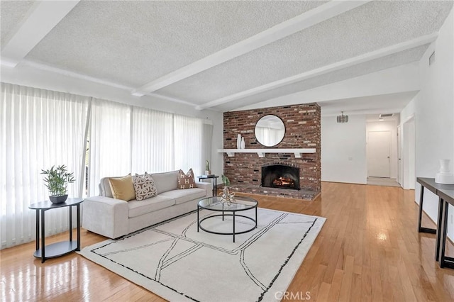 living room with a fireplace, a textured ceiling, light wood-type flooring, and lofted ceiling with beams