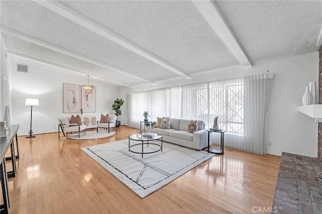 living room with hardwood / wood-style floors, a notable chandelier, beam ceiling, and a textured ceiling