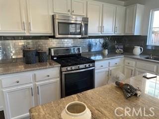 kitchen featuring backsplash, light stone countertops, white cabinets, and appliances with stainless steel finishes