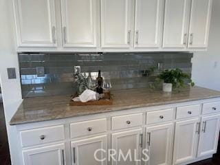 bar featuring backsplash, white cabinetry, and light stone countertops