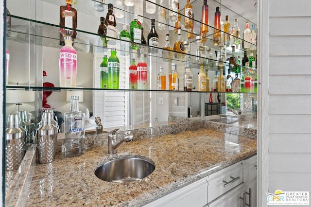 bar with white cabinets, stone countertops, and sink