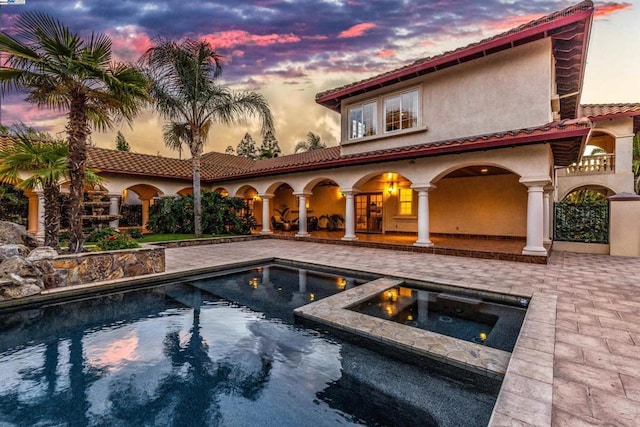 pool at dusk featuring a patio area and an in ground hot tub