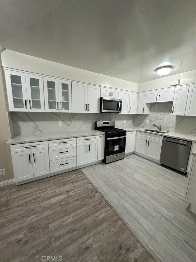 kitchen with white cabinetry, sink, decorative backsplash, appliances with stainless steel finishes, and light wood-type flooring