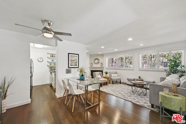 dining area with a textured ceiling, ceiling fan, a large fireplace, and dark hardwood / wood-style floors