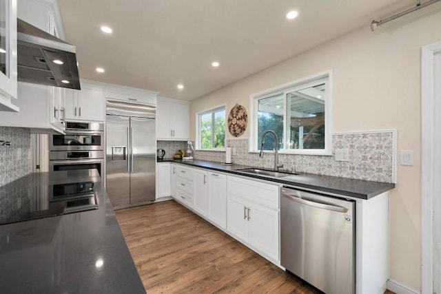 kitchen with wall chimney range hood, appliances with stainless steel finishes, sink, and white cabinetry