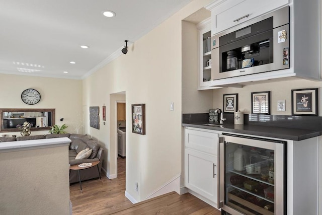 bar featuring wine cooler, light hardwood / wood-style floors, washer / clothes dryer, ornamental molding, and white cabinets