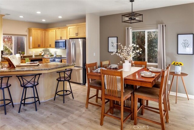 kitchen with pendant lighting, appliances with stainless steel finishes, light brown cabinetry, kitchen peninsula, and light hardwood / wood-style flooring