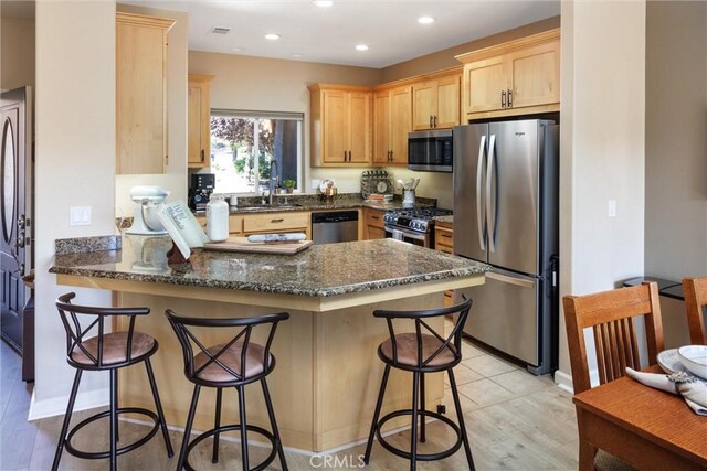 kitchen with stainless steel appliances, dark stone counters, sink, a kitchen breakfast bar, and kitchen peninsula