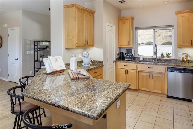 kitchen featuring a kitchen bar, dark stone counters, light brown cabinetry, sink, and stainless steel dishwasher