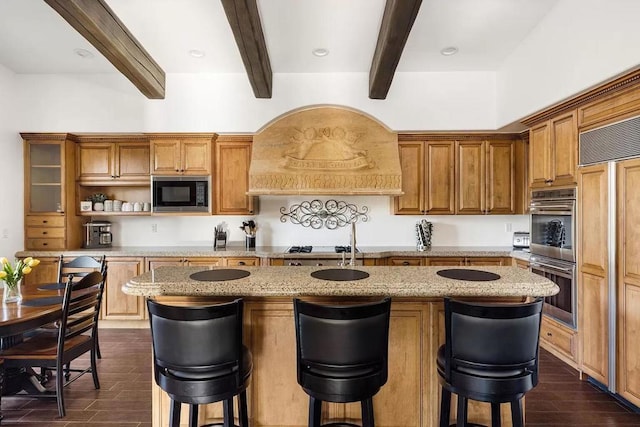 kitchen featuring beam ceiling, a kitchen island with sink, appliances with stainless steel finishes, and dark wood-type flooring