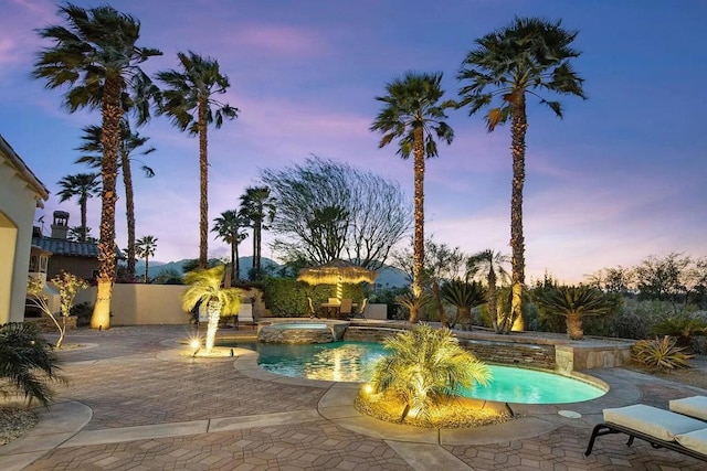 pool at dusk with an in ground hot tub and a patio