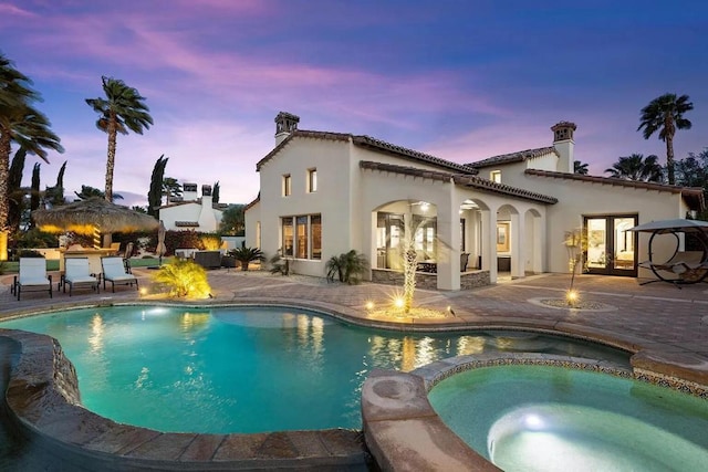 pool at dusk with an in ground hot tub, a patio, and french doors