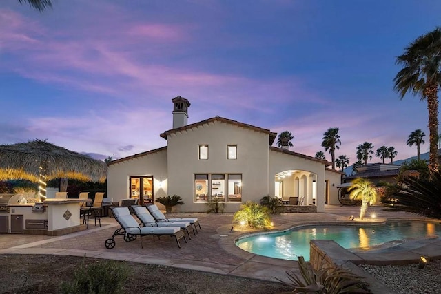 back house at dusk with an outdoor kitchen and a patio area