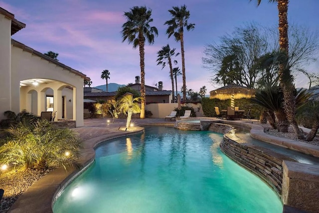 pool at dusk with a patio area and an in ground hot tub