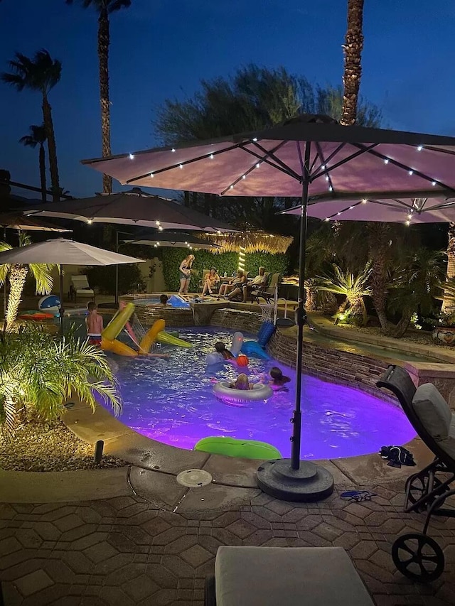 pool at night featuring a patio