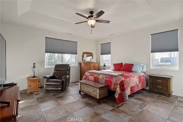 bedroom with a raised ceiling, multiple windows, and ceiling fan