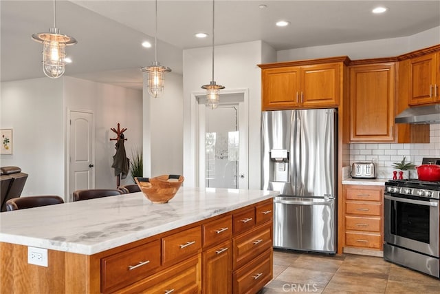 kitchen featuring tasteful backsplash, hanging light fixtures, a kitchen island, appliances with stainless steel finishes, and light stone counters