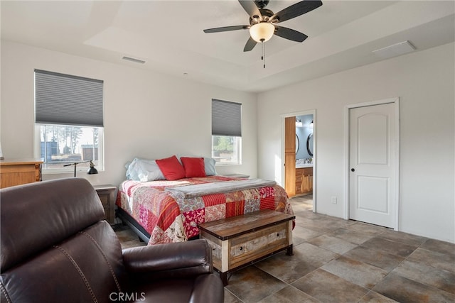 bedroom with ensuite bath, a tray ceiling, and ceiling fan