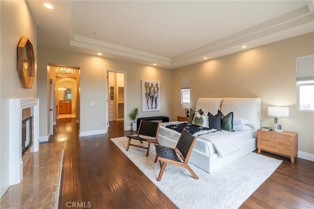 bedroom with a tray ceiling, a high end fireplace, and dark hardwood / wood-style floors