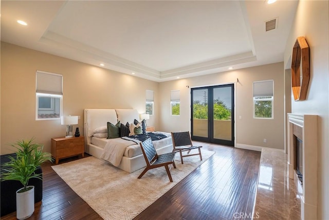 bedroom featuring access to exterior, hardwood / wood-style floors, and a tray ceiling