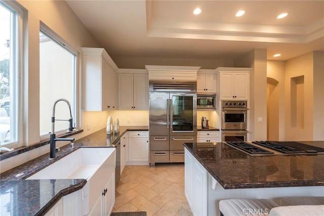 kitchen with white cabinets, built in appliances, a wealth of natural light, and dark stone counters