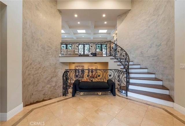 stairway featuring beam ceiling, a skylight, a high ceiling, coffered ceiling, and tile patterned floors