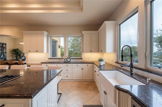 kitchen featuring white cabinets, dark stone countertops, sink, and backsplash