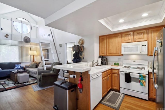 kitchen with light hardwood / wood-style floors, kitchen peninsula, a tray ceiling, and white appliances