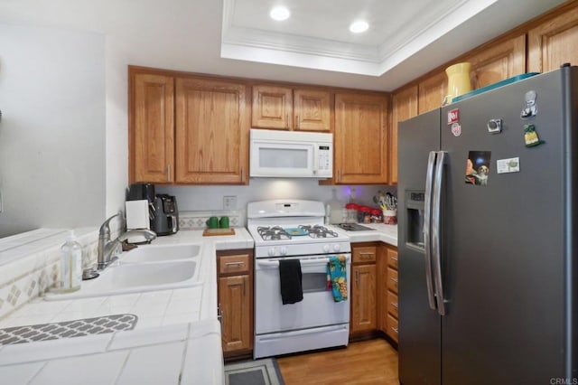 kitchen with white appliances, sink, tile countertops, a raised ceiling, and light hardwood / wood-style floors