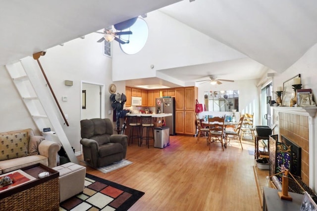 living room with a high ceiling, a tiled fireplace, light wood-type flooring, and ceiling fan