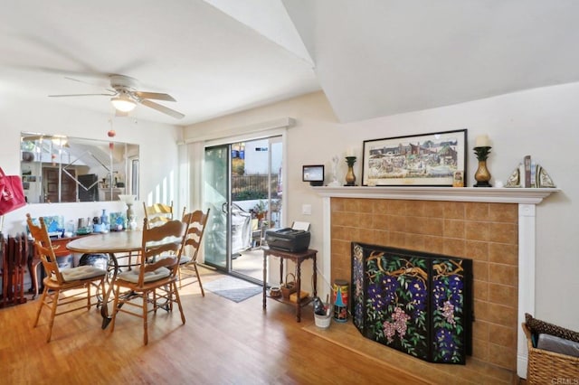 dining space featuring a tiled fireplace, wood-type flooring, and ceiling fan