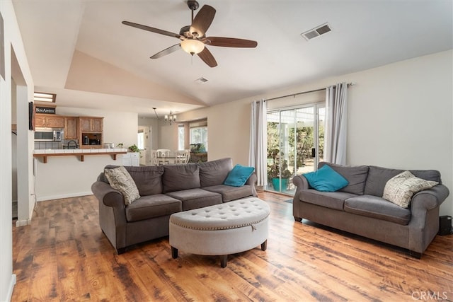 living room featuring dark hardwood / wood-style floors, ceiling fan with notable chandelier, and vaulted ceiling