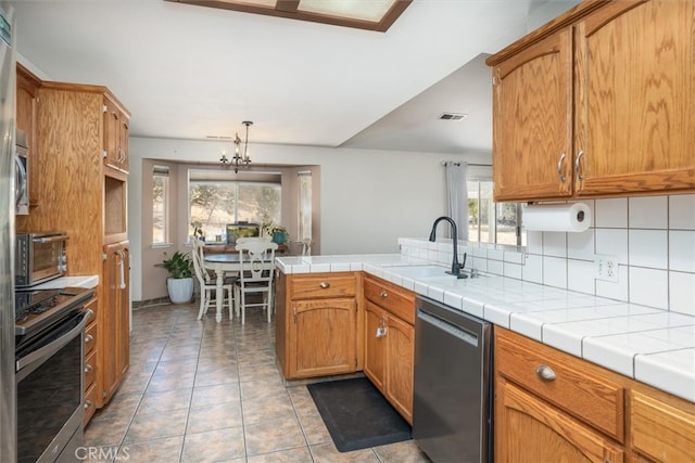 kitchen with decorative backsplash, kitchen peninsula, sink, an inviting chandelier, and appliances with stainless steel finishes