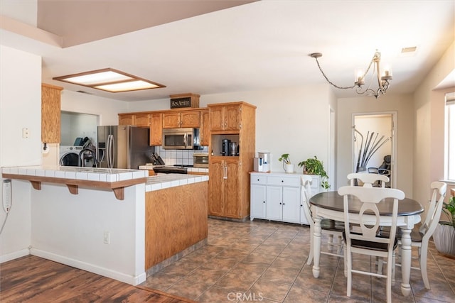 kitchen featuring washer and clothes dryer, tile counters, kitchen peninsula, a chandelier, and appliances with stainless steel finishes