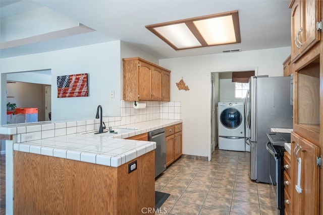 kitchen featuring washer / dryer, sink, kitchen peninsula, stainless steel appliances, and tile counters