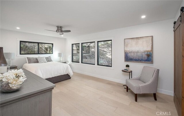 bedroom featuring ceiling fan, a barn door, and light wood-type flooring